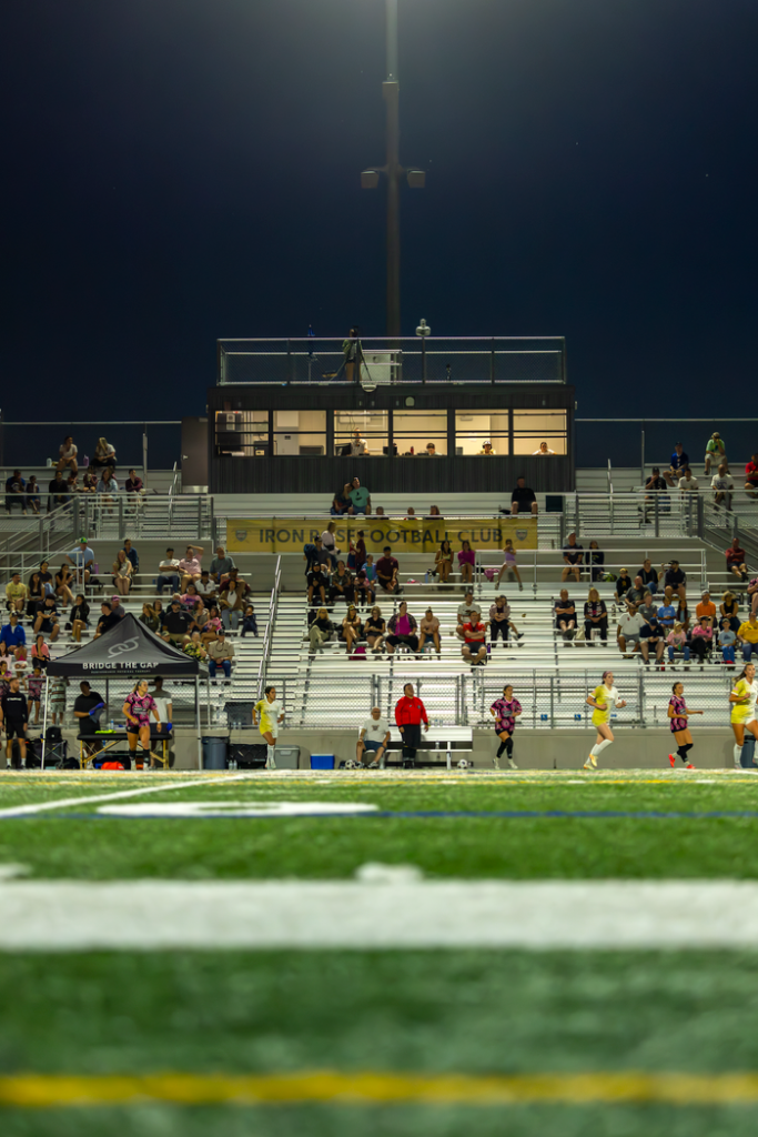 Football stadium under lights at night with spectators in the stands.
