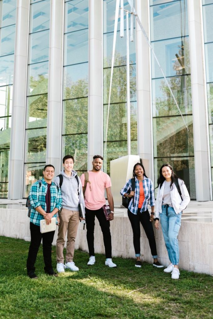 A diverse group of happy students standing outside a modern campus building.